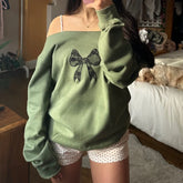 Person wearing a green sweatshirt with a bow design in a casual indoor setting